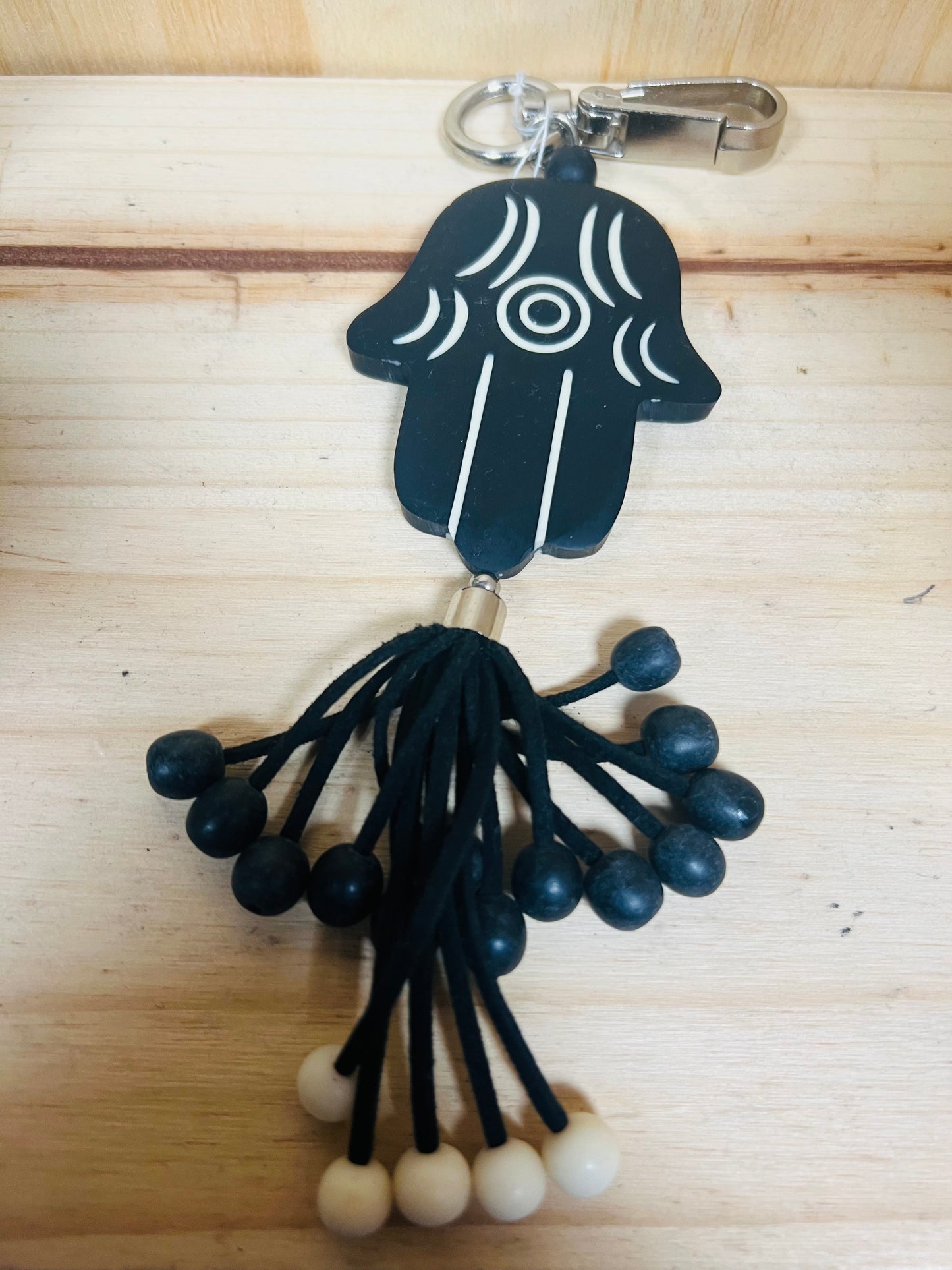 Black Hamsa hand keychain with tassels on a wooden surface