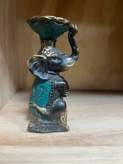 Decorative elephant figurine with a bowl on its trunk, made of metal, on a wooden surface.