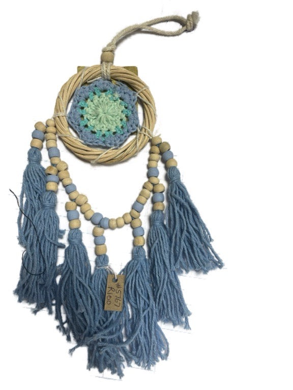 Decorative wall hanging with blue tassels and a crocheted center on a white background