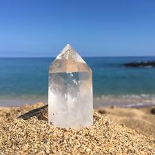 Clear crystal pyramid on a pebble beach with ocean and blue sky in the background